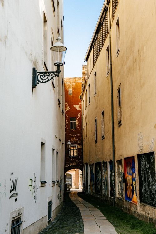 Free An urban narrow alley with graffiti-covered walls between aged European buildings, evoking an artistic city vibe. Stock Photo