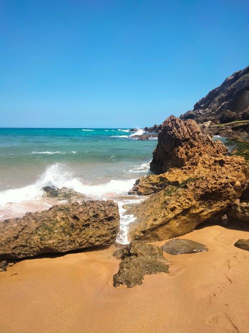 Free Vibrant beach scene featuring rocky shoreline with turquoise waves under a clear sky. Perfect for travel inspirations. Stock Photo