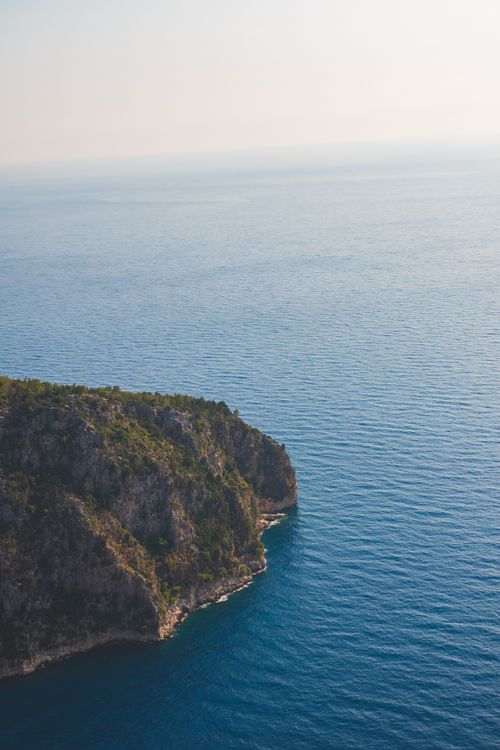 Free Stunning aerial view of a rocky coastal cliffside against a vast blue ocean under a bright sky. Stock Photo