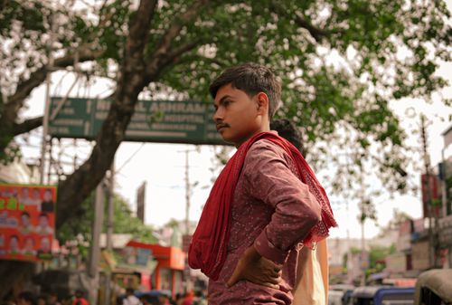 Free Young man standing confidently in a bustling city street with trees and traffic. Stock Photo