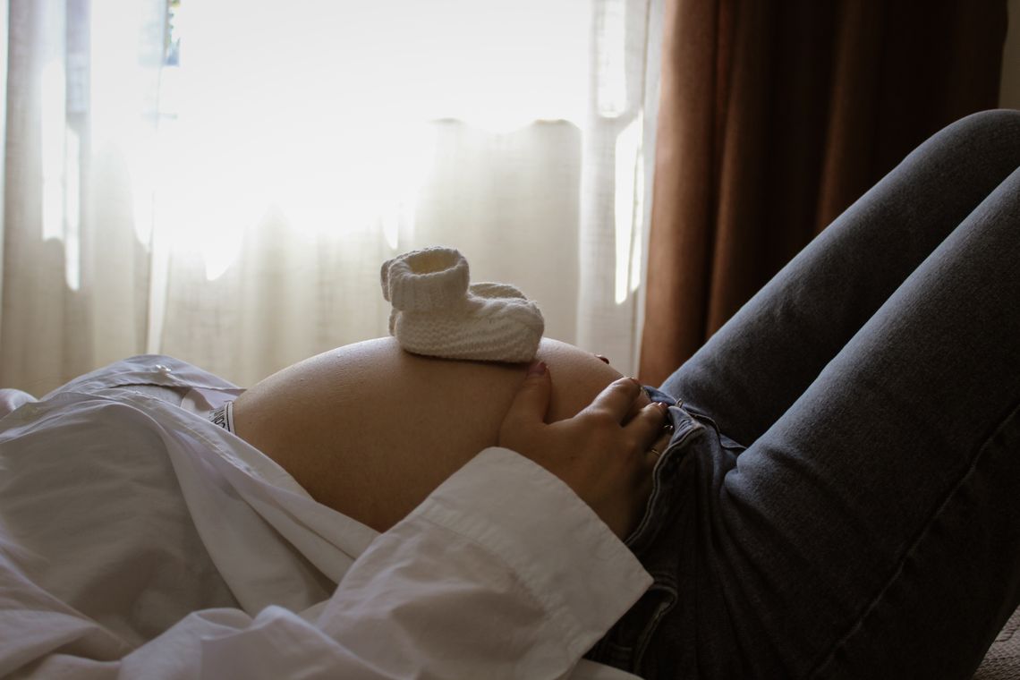 Pregnant woman resting with small baby shoes placed gently on her belly