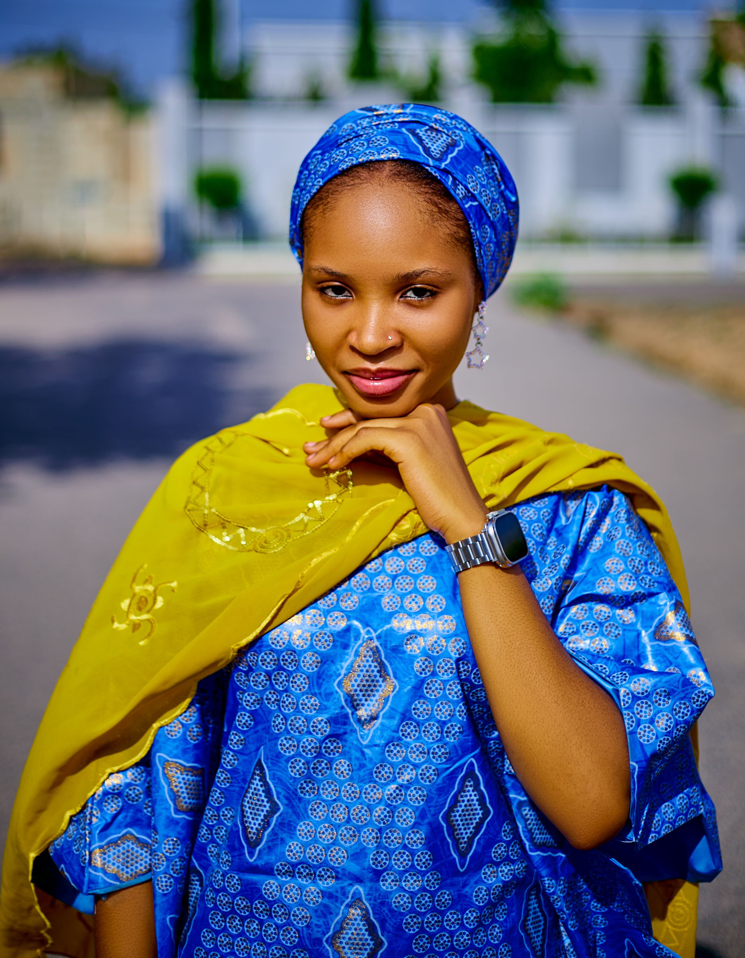 A young woman in colorful traditional clothing smiles outdoors on a sunny day.