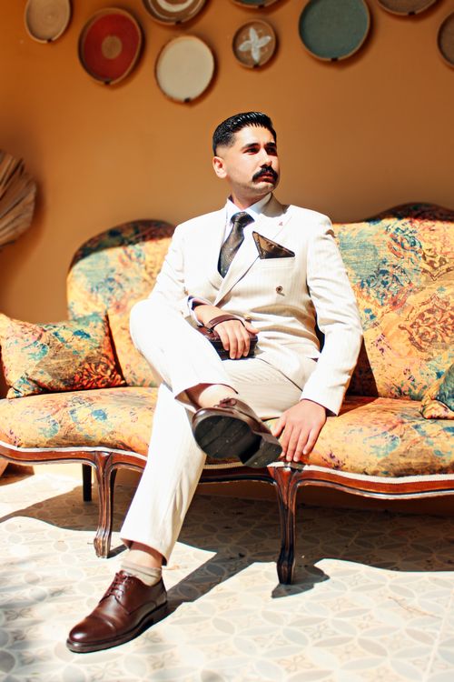 Free Stylish man in white suit sitting on vintage sofa with artistic decor. Perfect blend of modern elegance and classic style. Stock Photo