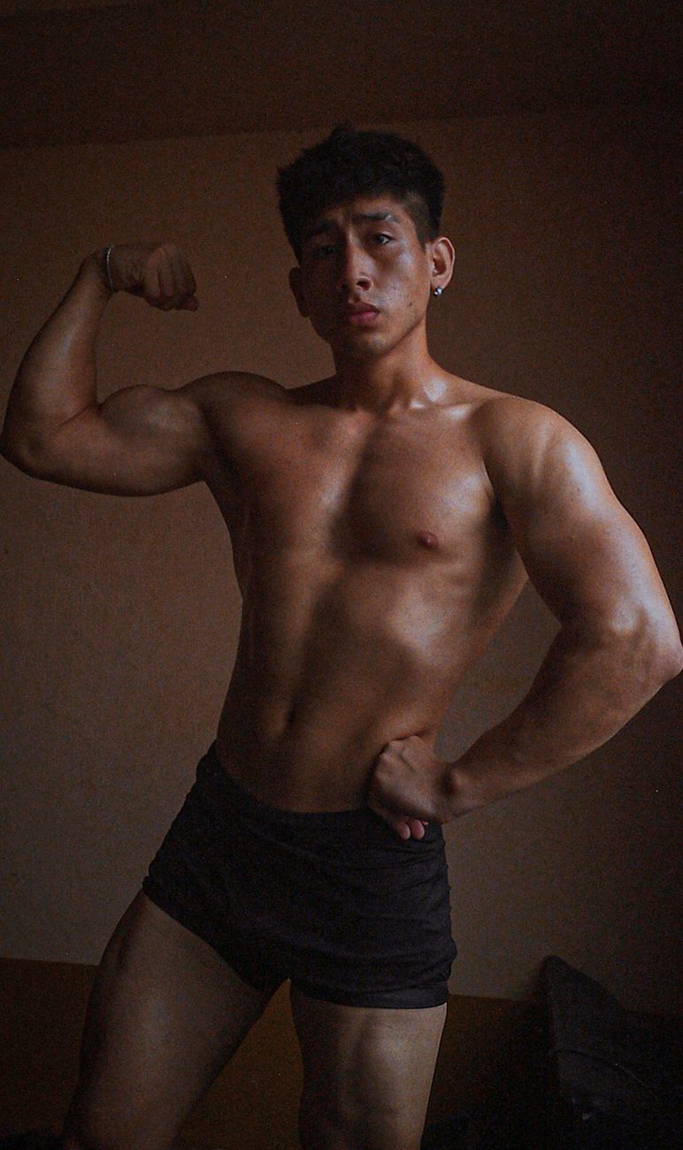 A muscular man flexing his arms indoors in Machala, Ecuador, showcasing strength and fitness.