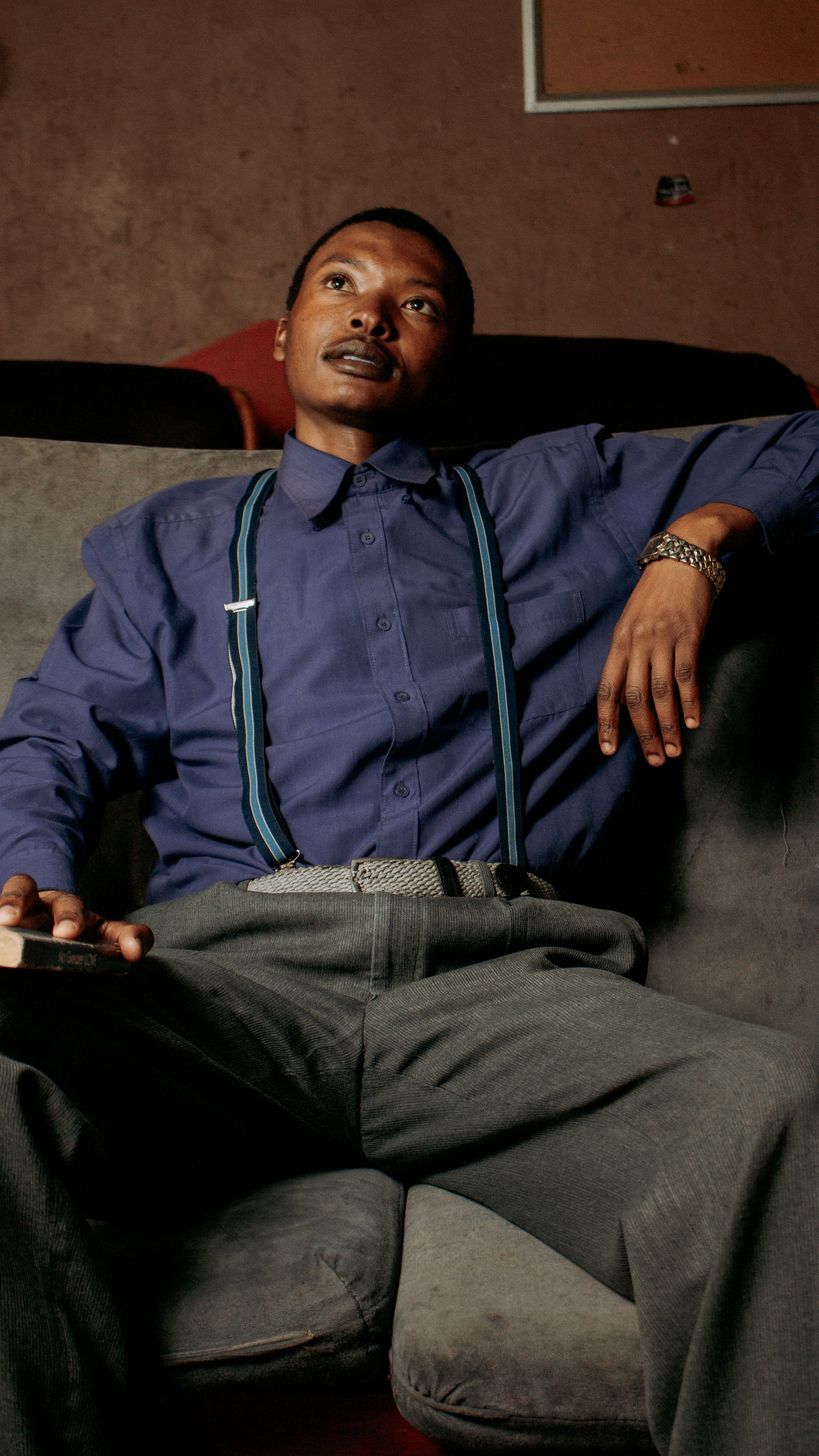 A man in suspenders sits thoughtfully on a sofa, creating a relaxed indoor ambiance.