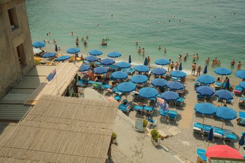 Free Vibrant beach scene with blue umbrellas along the Amalfi Coast, perfect for summer travel. Stock Photo