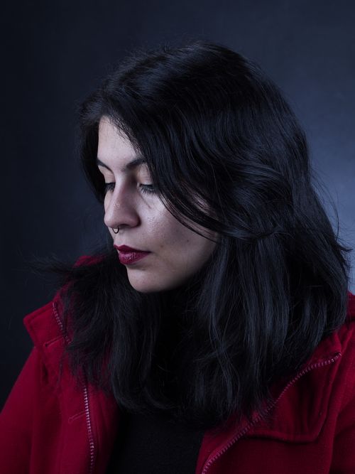 Free Close-up portrait of a woman with long black hair and red coat, evoking a moody atmosphere. Stock Photo
