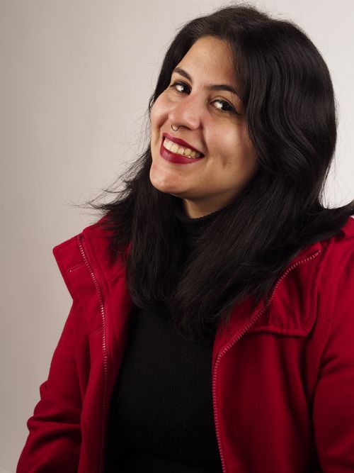 Free Cheerful woman in a red jacket, smiling warmly against a plain backdrop. Stock Photo