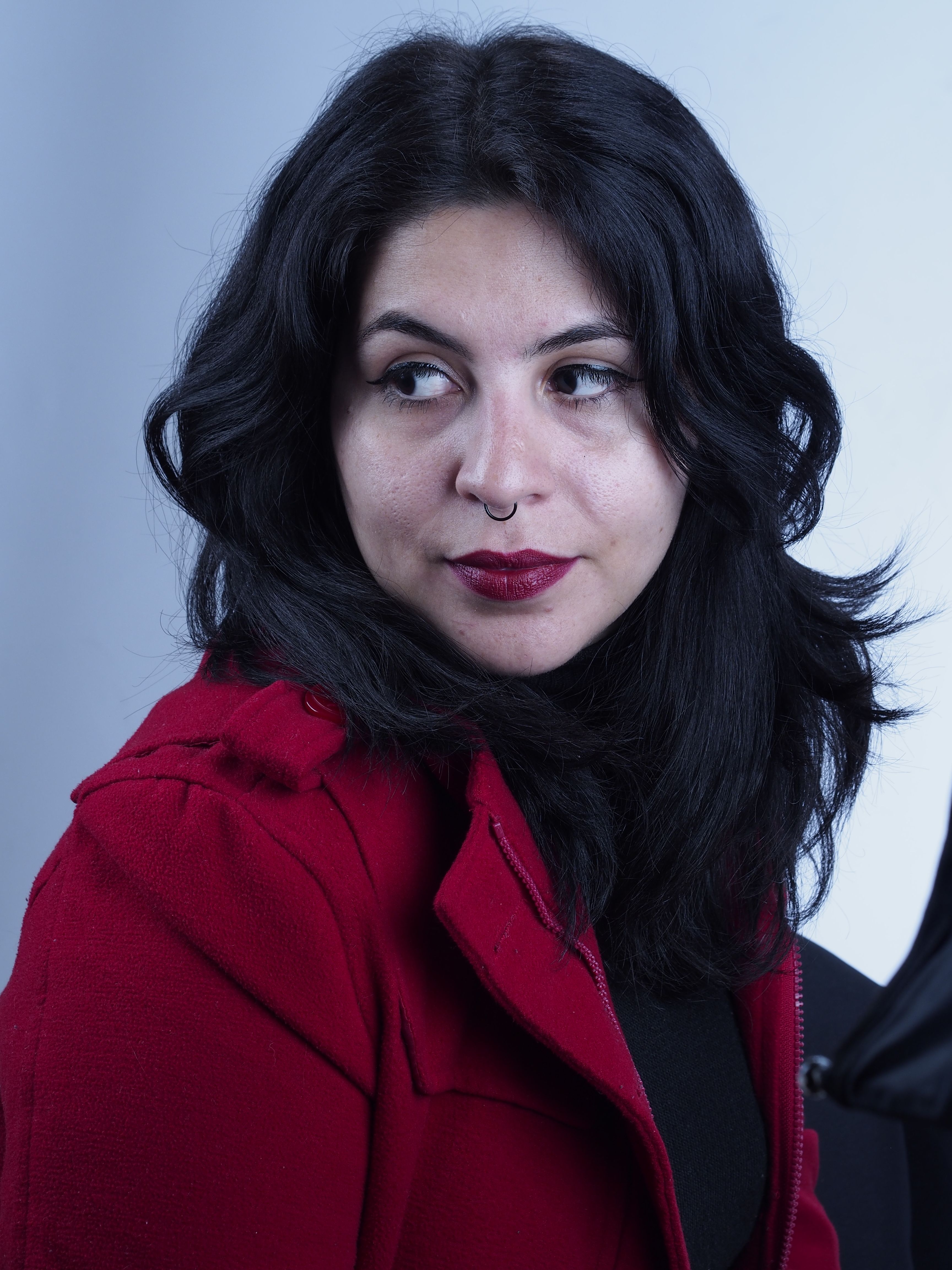 Stylish woman in a red coat and dark hair looking to the side, studio portrait.