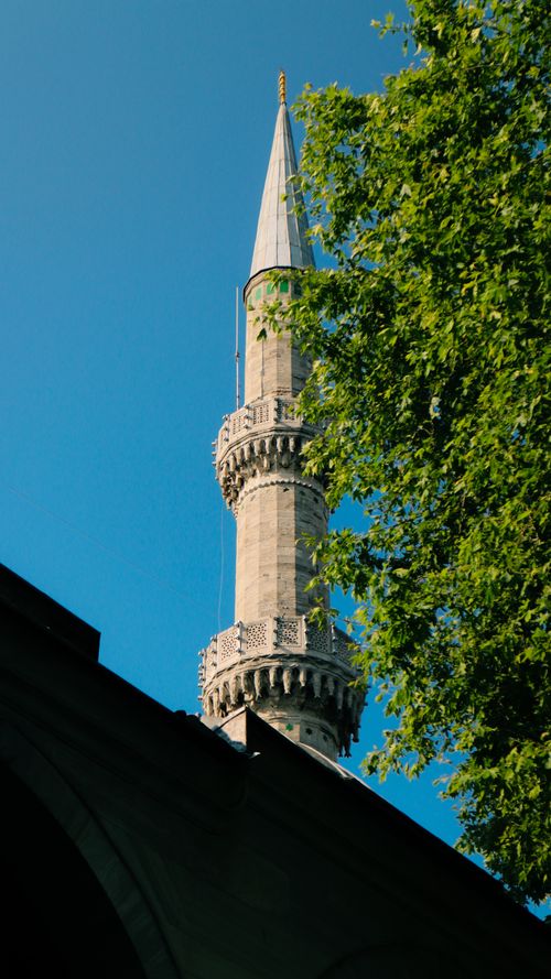 Free A beautiful mosque minaret framed by lush green trees under a clear blue sky. Stock Photo