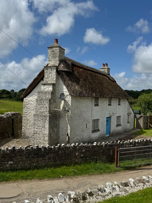 Free Picturesque thatched cottage surrounded by lush countryside under a bright blue sky. Stock Photo
