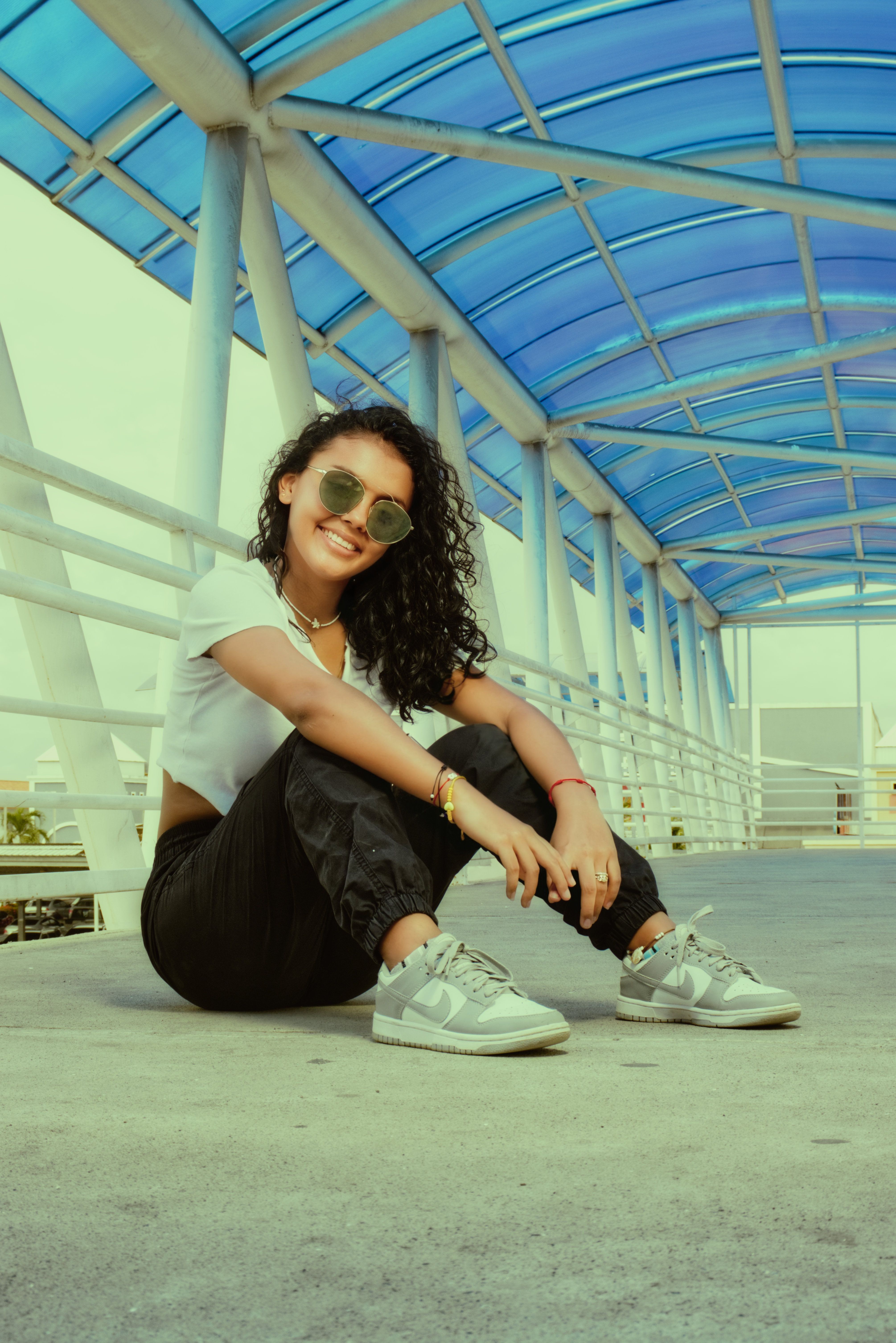 Stylish woman in casual attire sitting on a blue-tinted bridge. Fashion-forward and relaxed.