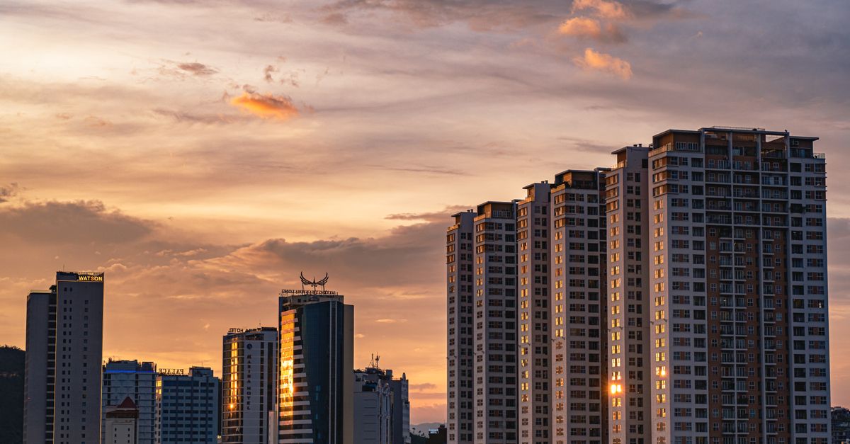 Urban skyline with tall buildings at sunset, reflecting warm colors in the sky.