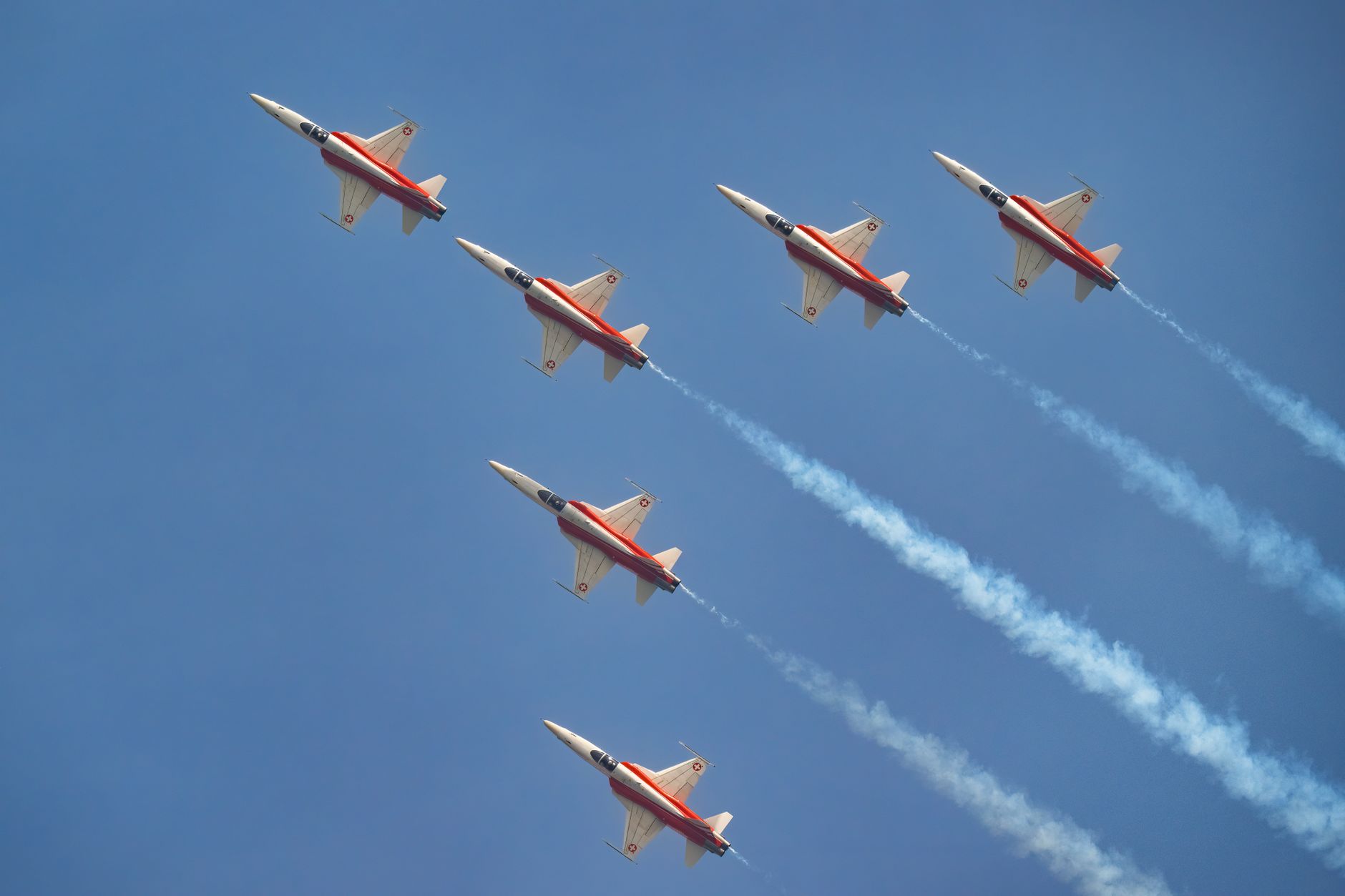 Six fighter jets in tight formation leave trails in bright blue sky, showcasing aviation precision.