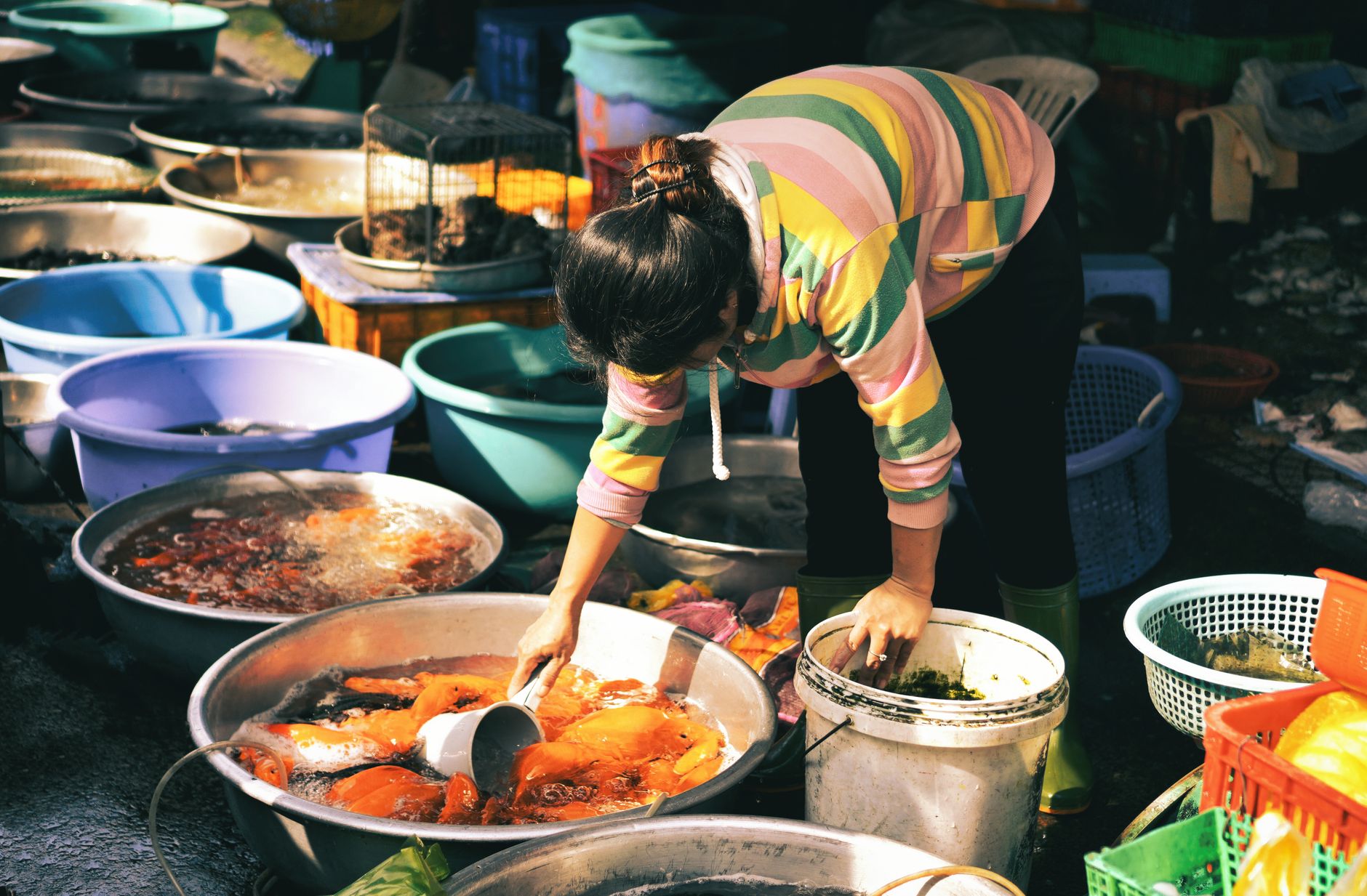 Woman at a bustling Vietnamese fish market tending to fresh seafood in colorful basins.