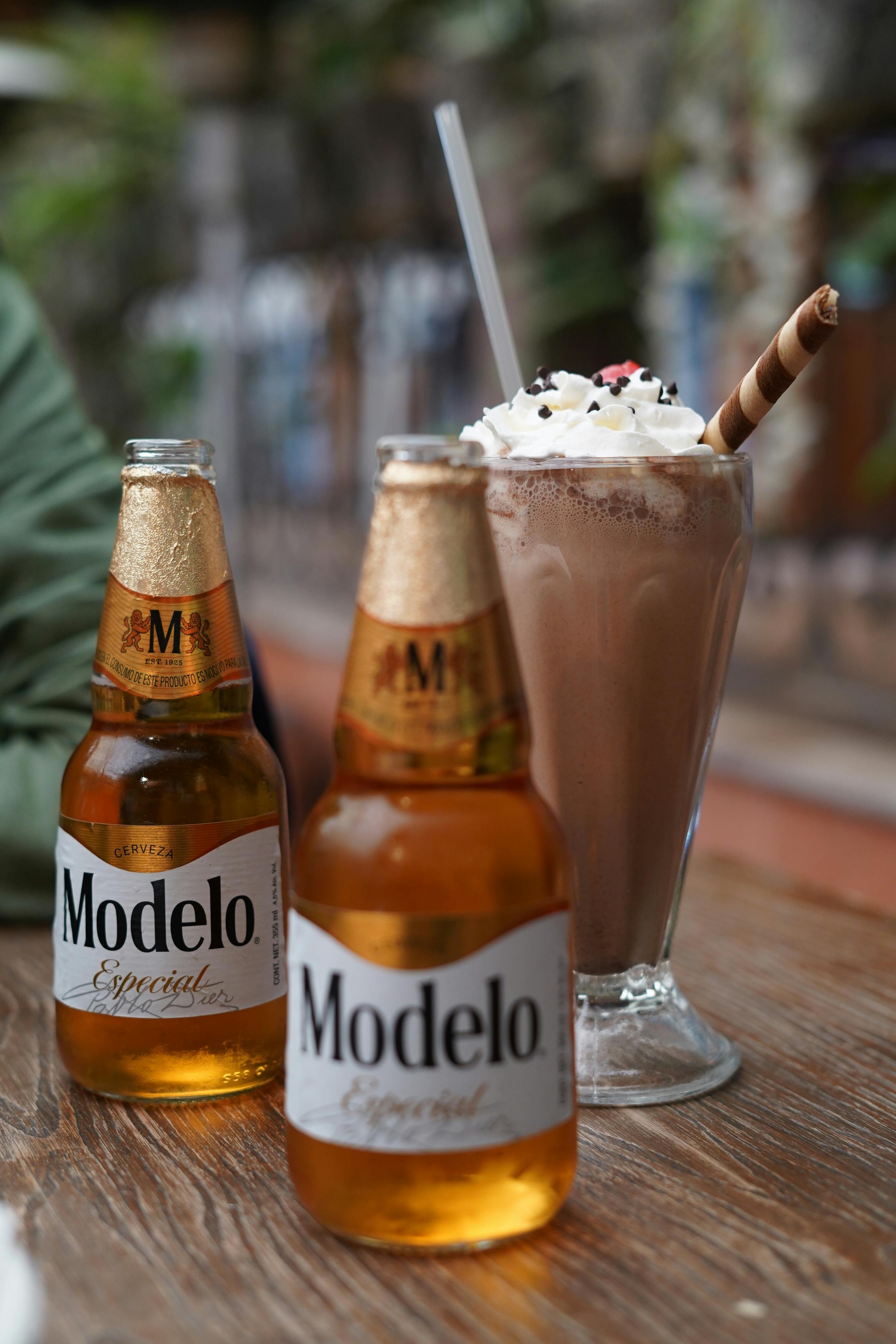 Gratuit Deux bouteilles de bière et un milkshake au chocolat sur une table à l'extérieur, parfait pour une journée de détente. Photos