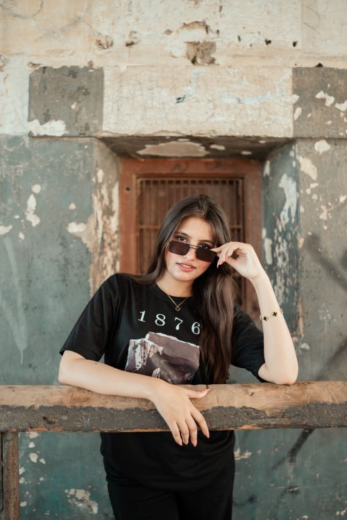 Free A young woman posing confidently outdoors, wearing sunglasses and a graphic t-shirt. Stock Photo