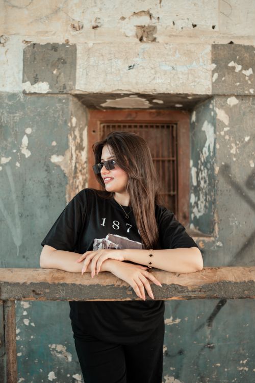 Free Stylish woman in sunglasses leaning on a rustic railing against a weathered wall. Stock Photo