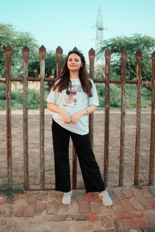 Free Casual portrait of a young woman standing by a rustic fence with trees in the background. Stock Photo