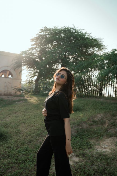 Free A fashionable woman in sunglasses poses against a sunny outdoor backdrop. Stock Photo