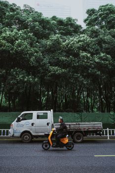 Dynamic urban scene featuring a moving scooter and parked truck against a lush green backdrop.
