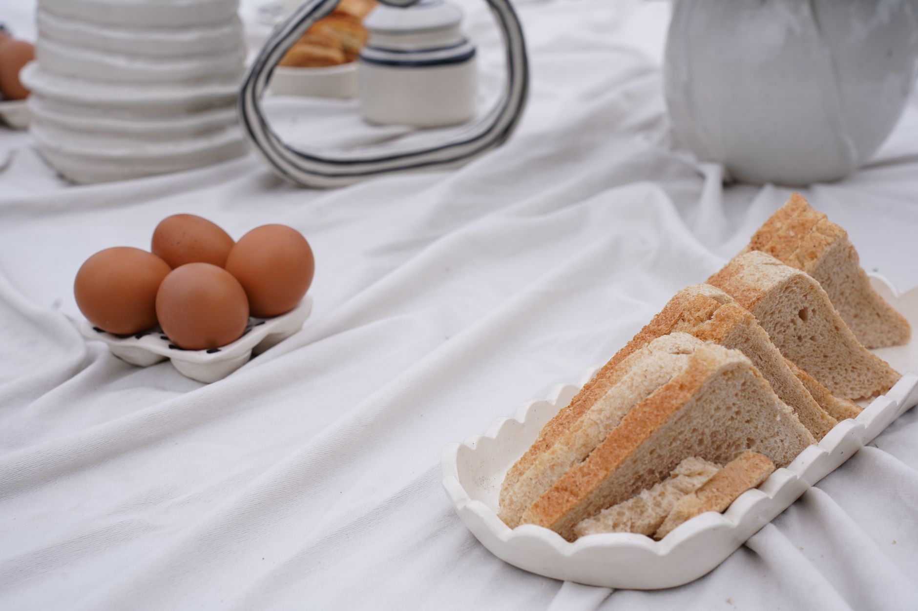 Minimalistic breakfast setup featuring sliced bread and eggs on a soft white cloth. Perfect for lifestyle inspiration.