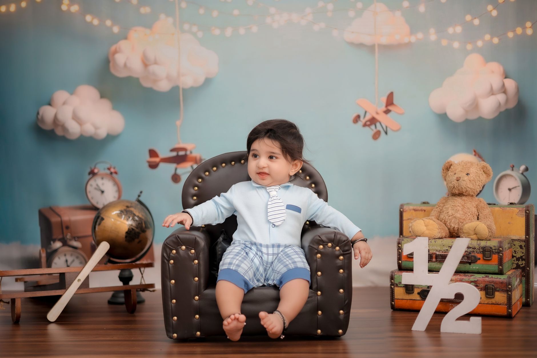 Adorable baby sits in vintage-themed photo shoot with toys and decor.