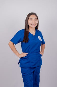 Professional nurse in blue scrubs posing confidently against a plain background.
