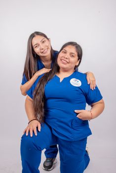 Two female medical professionals in blue uniforms posing confidently with friendly smiles in a studio setting.