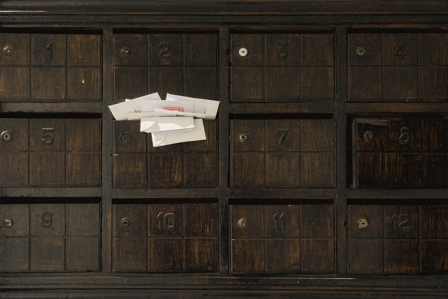 Old wooden mailbox showing numbered slots and inserted letters.