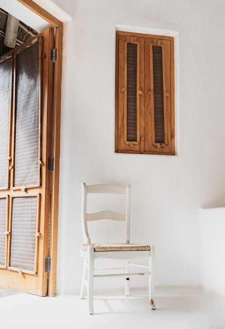 A serene white room featuring a wooden chair and rustic window design.