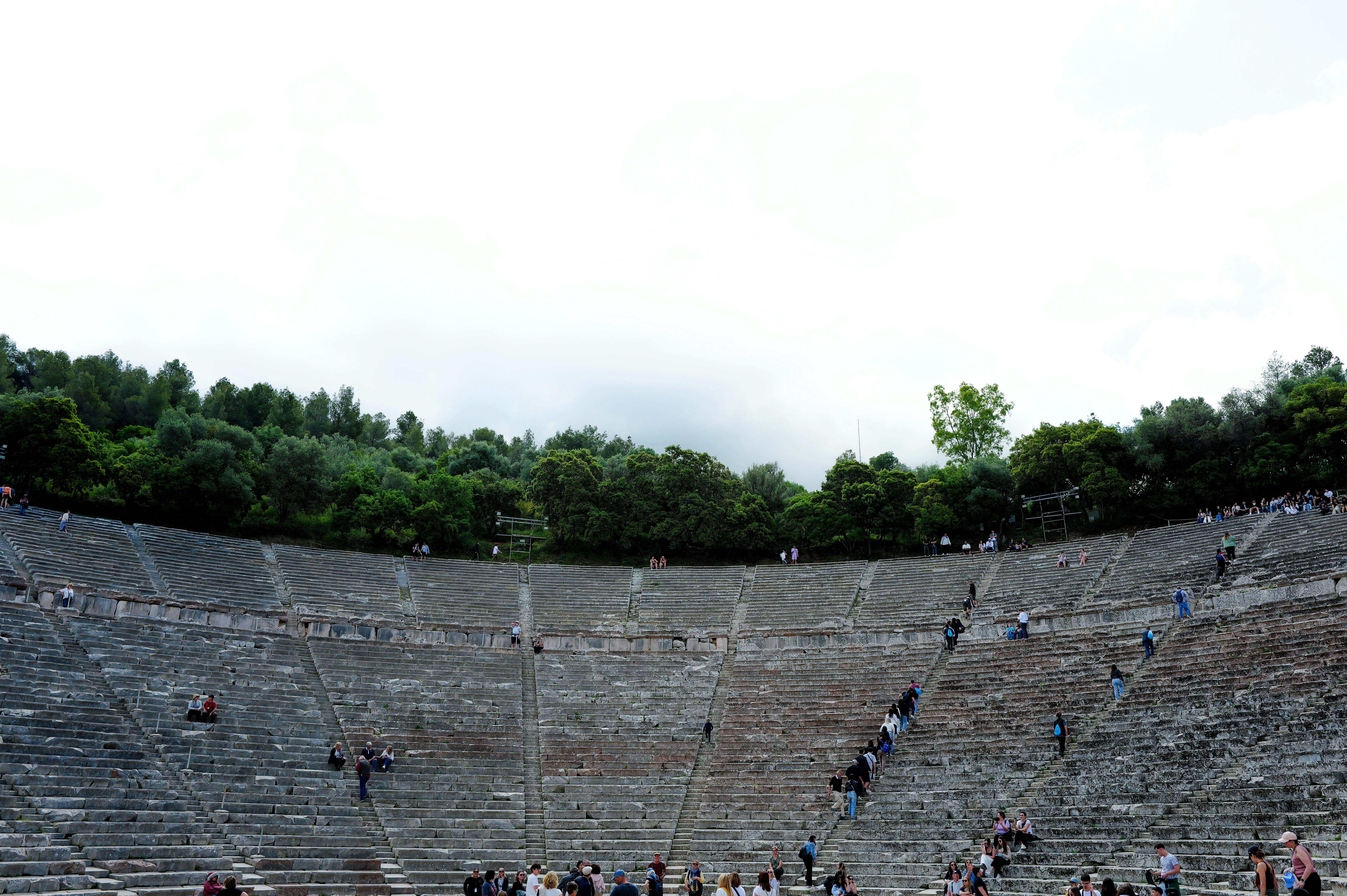 grátis Uma vista grande angular de um antigo teatro cercado por árvores exuberantes e um céu claro. Foto profissional