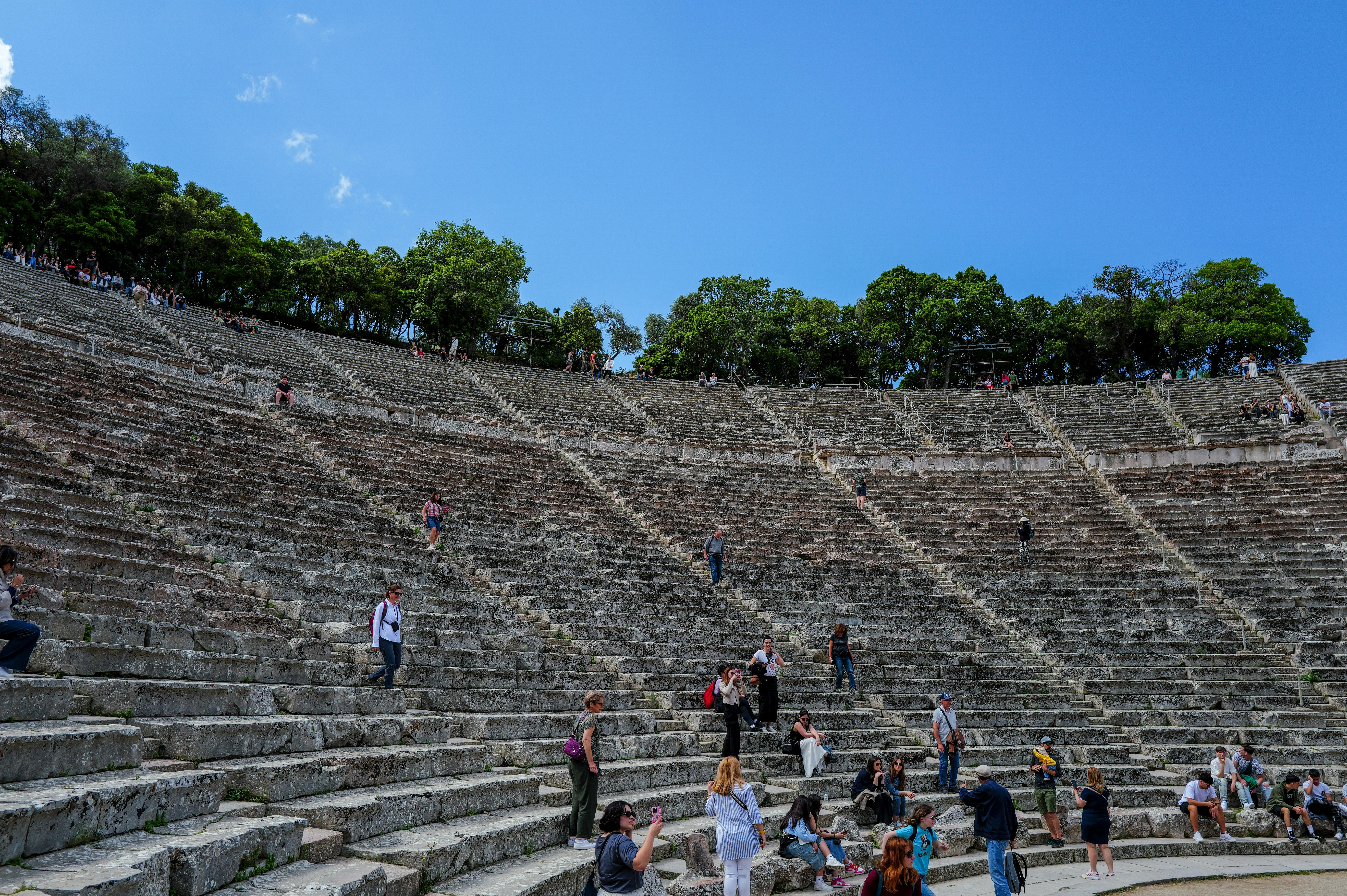 Zadarmo Návštevníci objavujú starobylý kamenný amfiteáter s bujnými stromami a žiarivo modrou oblohou nad hlavou. Fotka z fotobanky