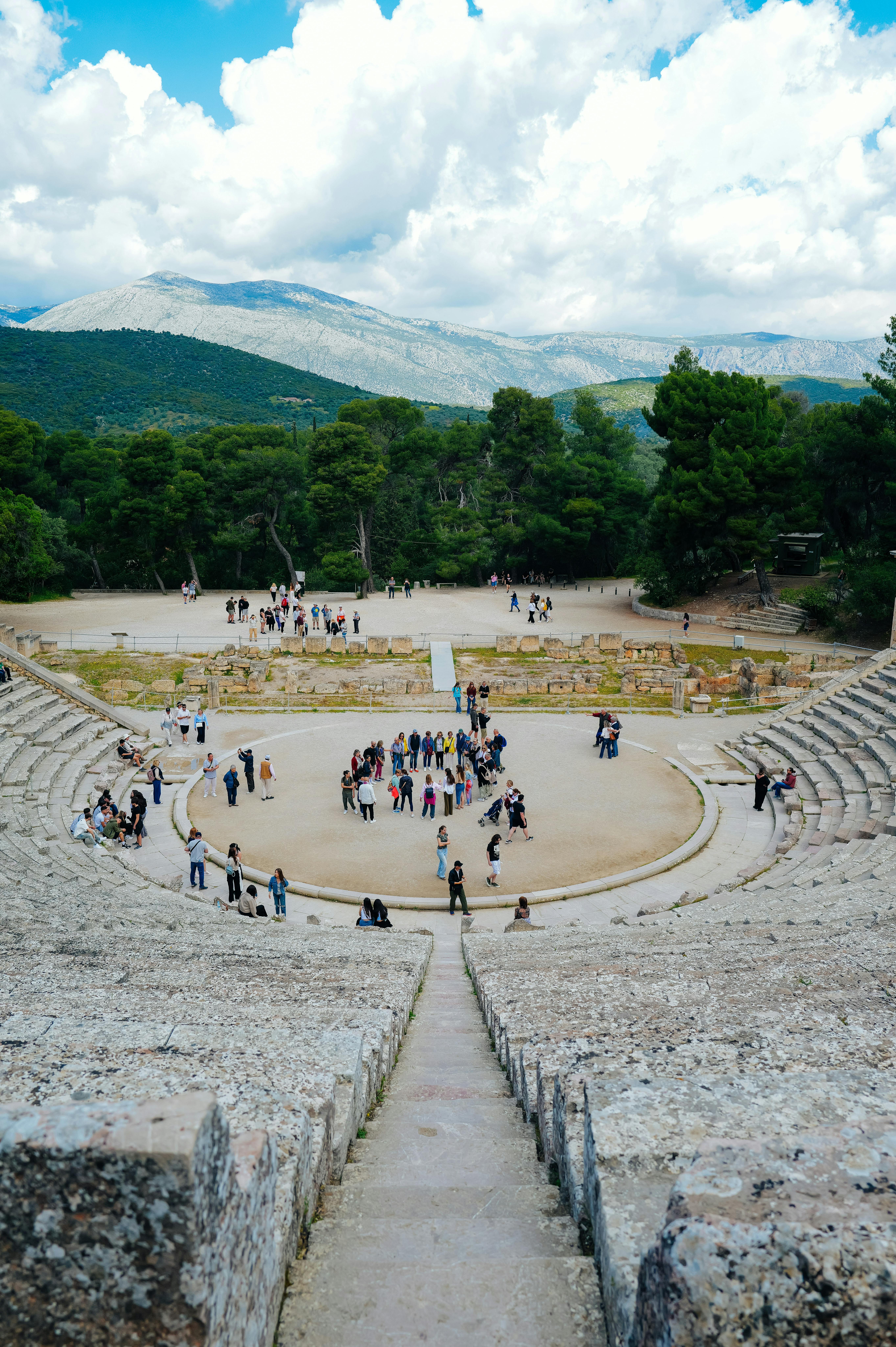 Ücretsiz Ziyaretçiler, güneşli bir günde yemyeşil bir çevreye kurulmuş antik bir Yunan amfi tiyatrosunda toplanıyor. Stok Fotoğraflar
