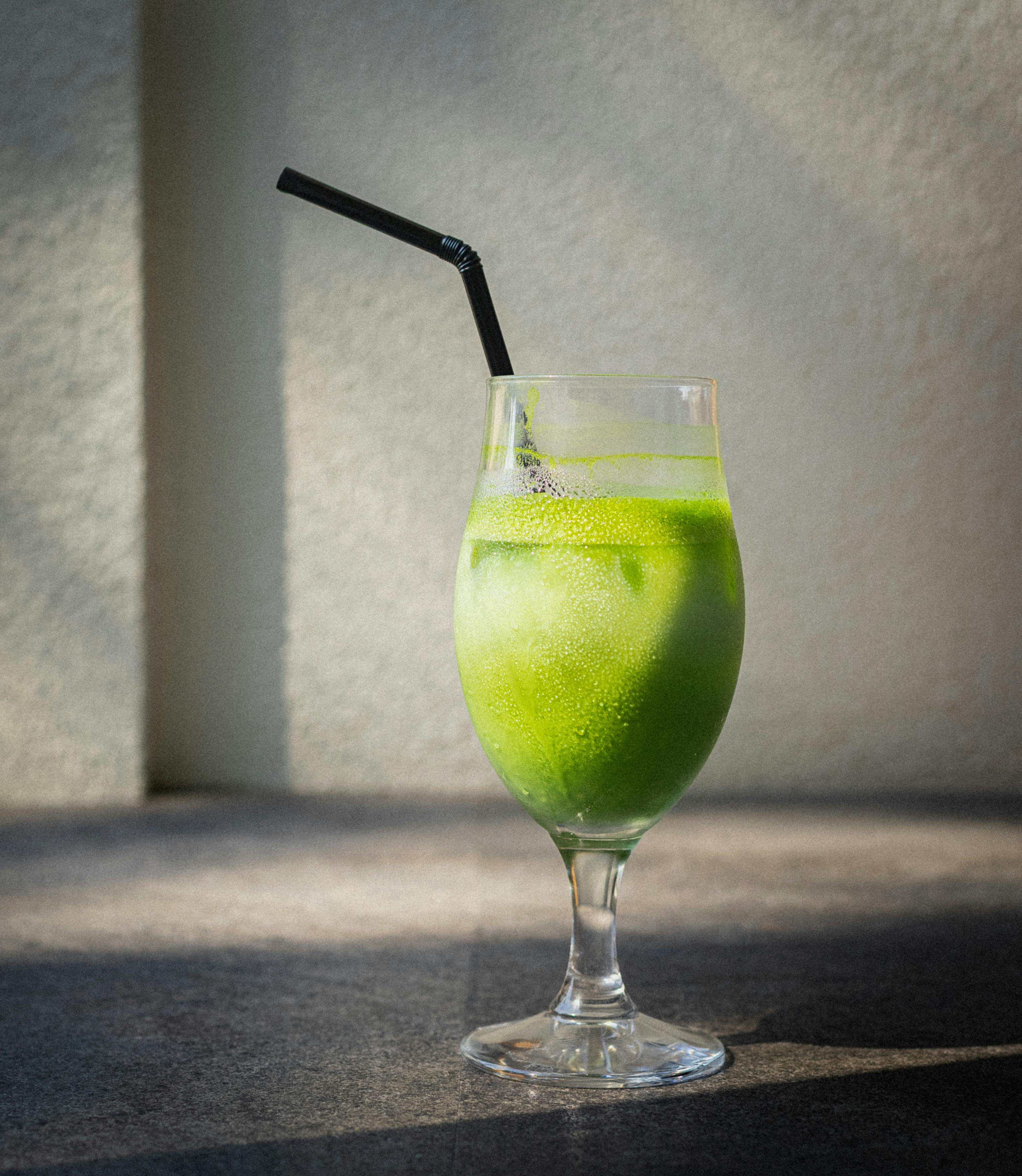 A refreshing iced matcha latte in a glass with ice cubes, cast in sunlight shadows indoors.