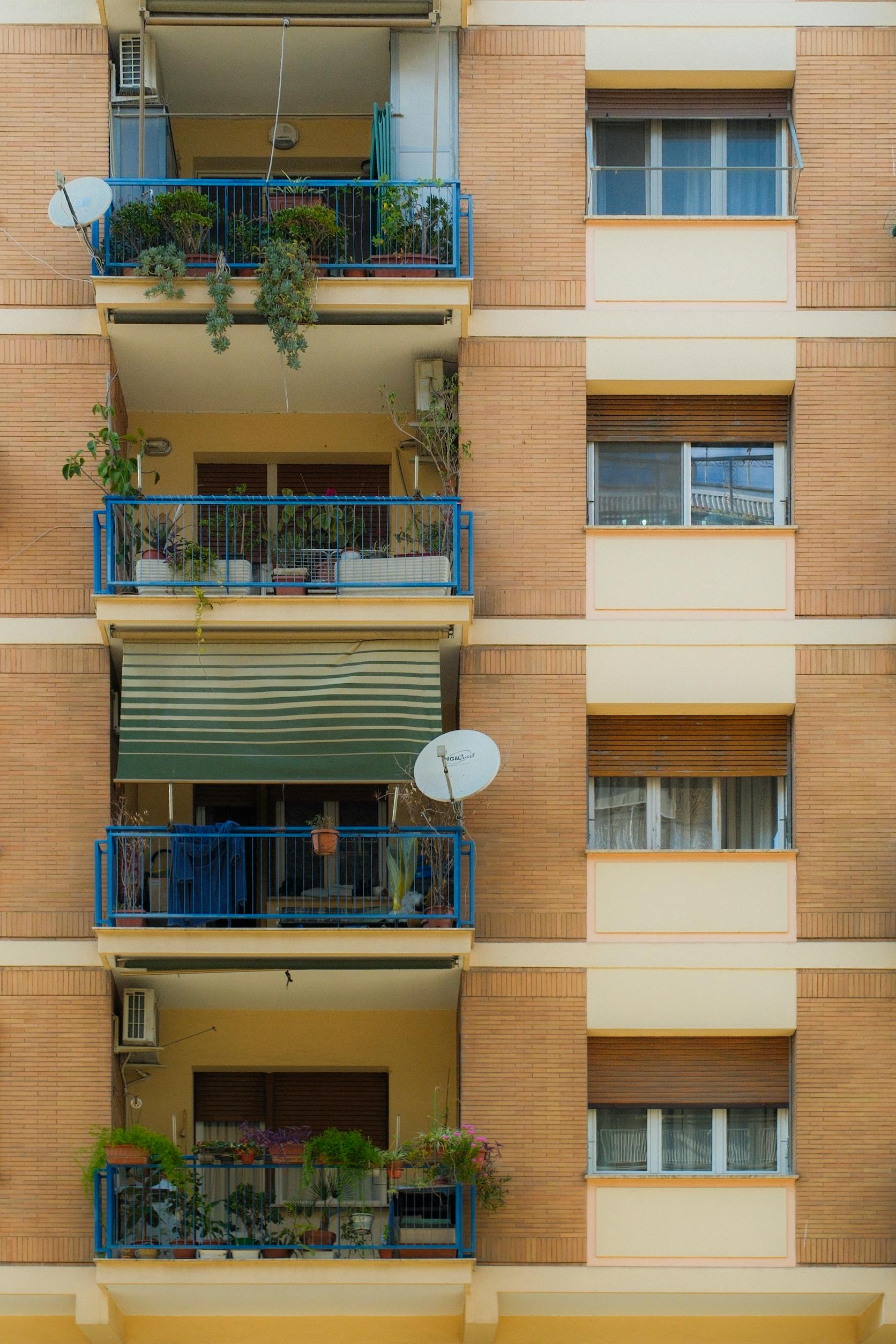 Vibrant apartment facade featuring balconies with plants and satellite dishes.