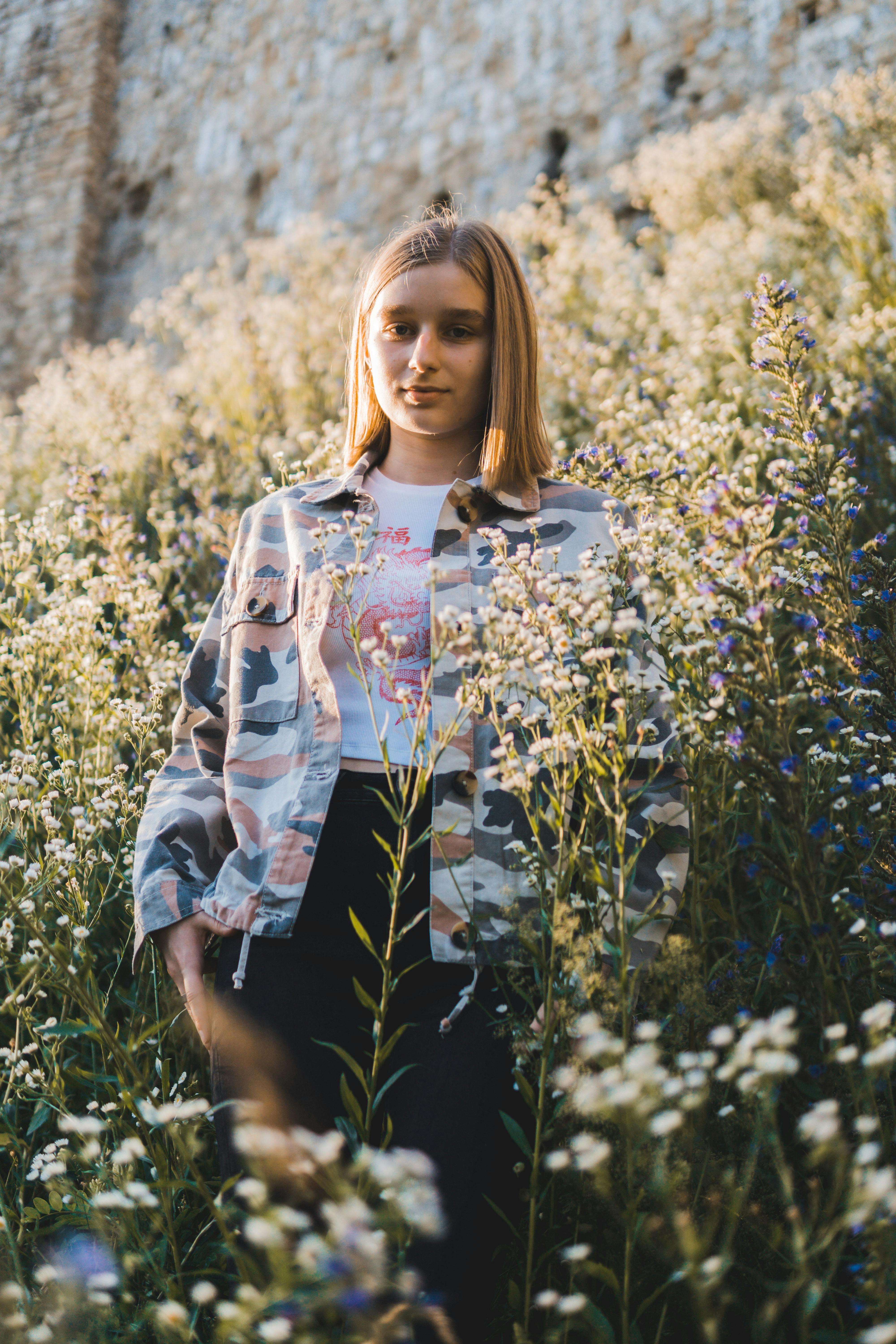 一名女子穿着迷彩夹克，站在阳光明媚的野花田里