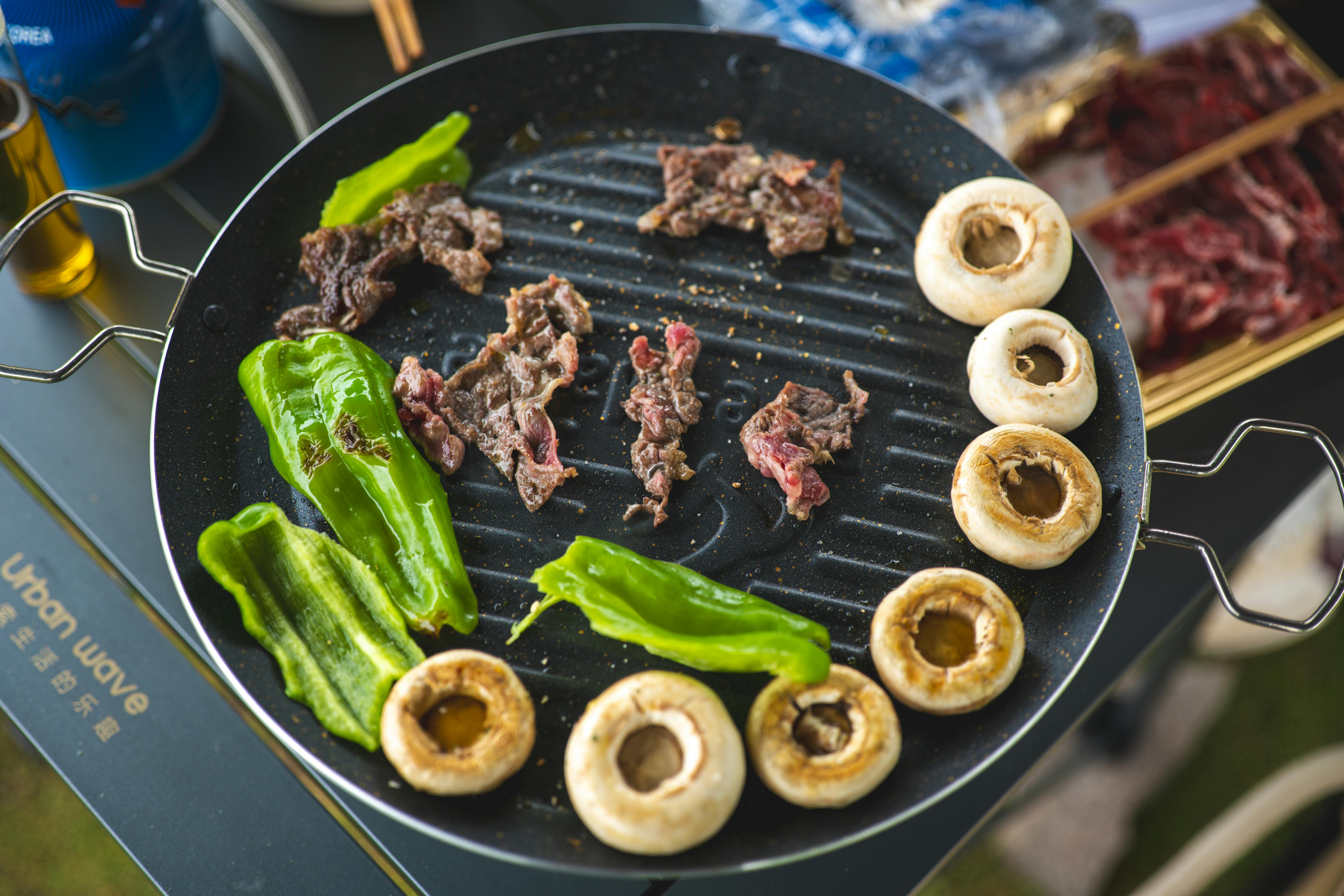 Sizzling beef, mushrooms, and green peppers on an outdoor grill, perfect for a summer barbecue.