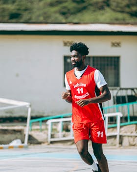 Basketball player in red jersey playing outdoors on a sunny day.