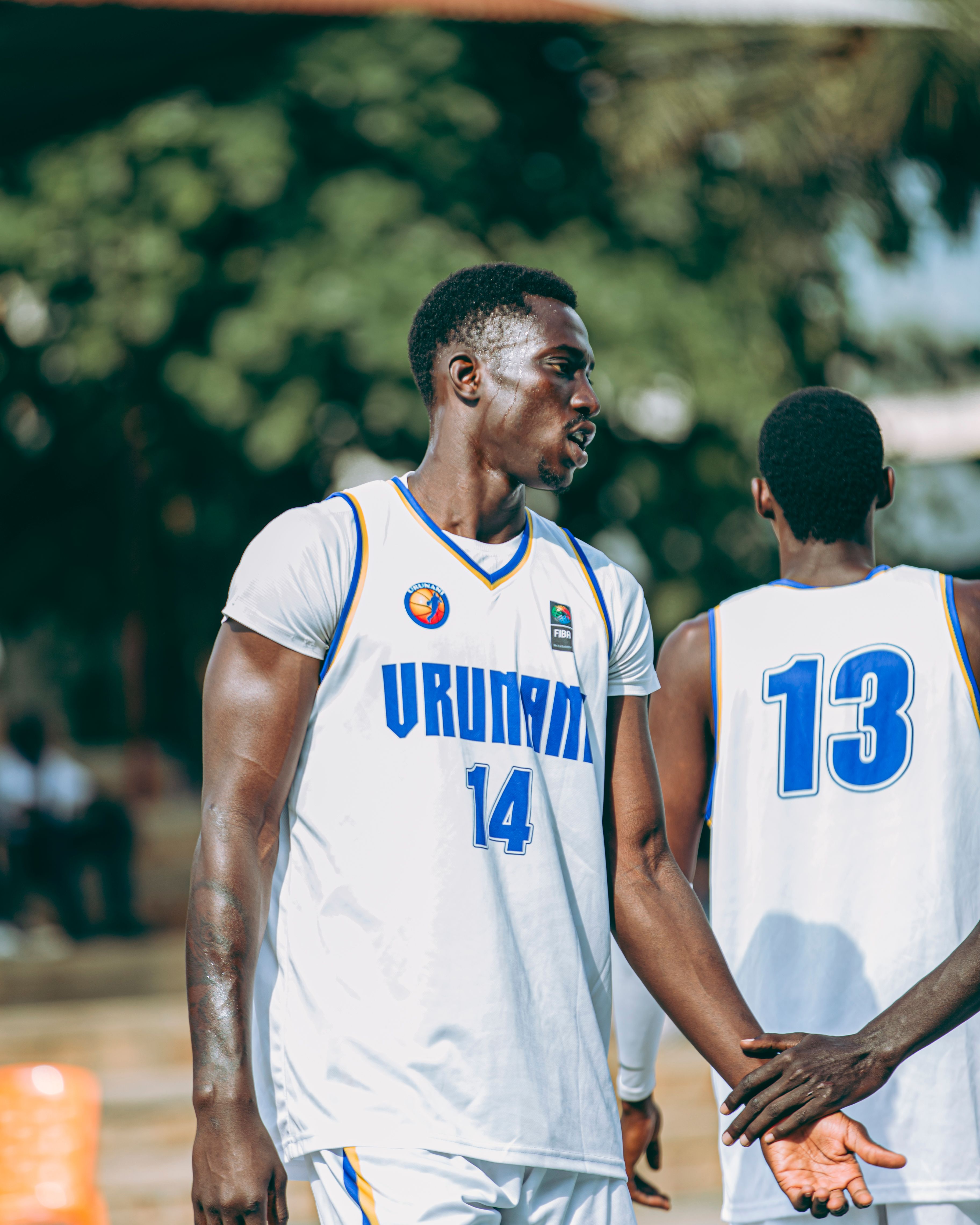 Two men playing outdoor basketball, wearing jerseys number 14 and 13.