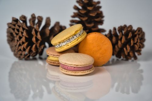 Free A selection of colorful French macarons paired with pinecones on a reflective white surface. Stock Photo