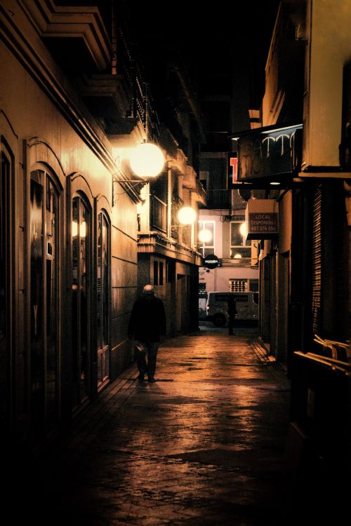 Free A lone figure walks down a beautifully lit street in Elche at night, offering a moody urban atmosphere. Stock Photo