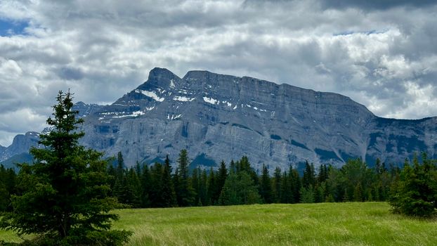 Scenic view of Canadian Rocky Mountains with lush green forest and cloudy sky.