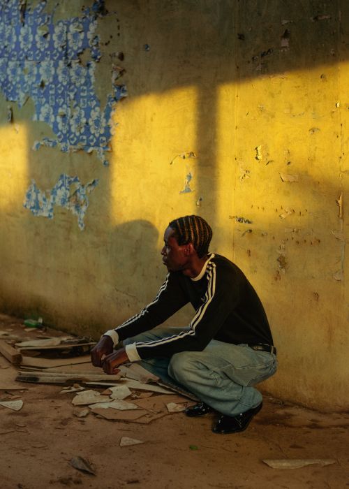Free Man crouching in sunlight against weathered wall in abandoned building. Stock Photo