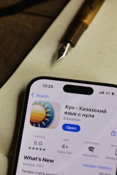 Smartphone displaying Kazakh language learning app on wooden desk with pen.