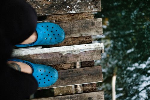 Free Close-up of a person in blue shoes standing on a rustic wooden pier above water. Stock Photo