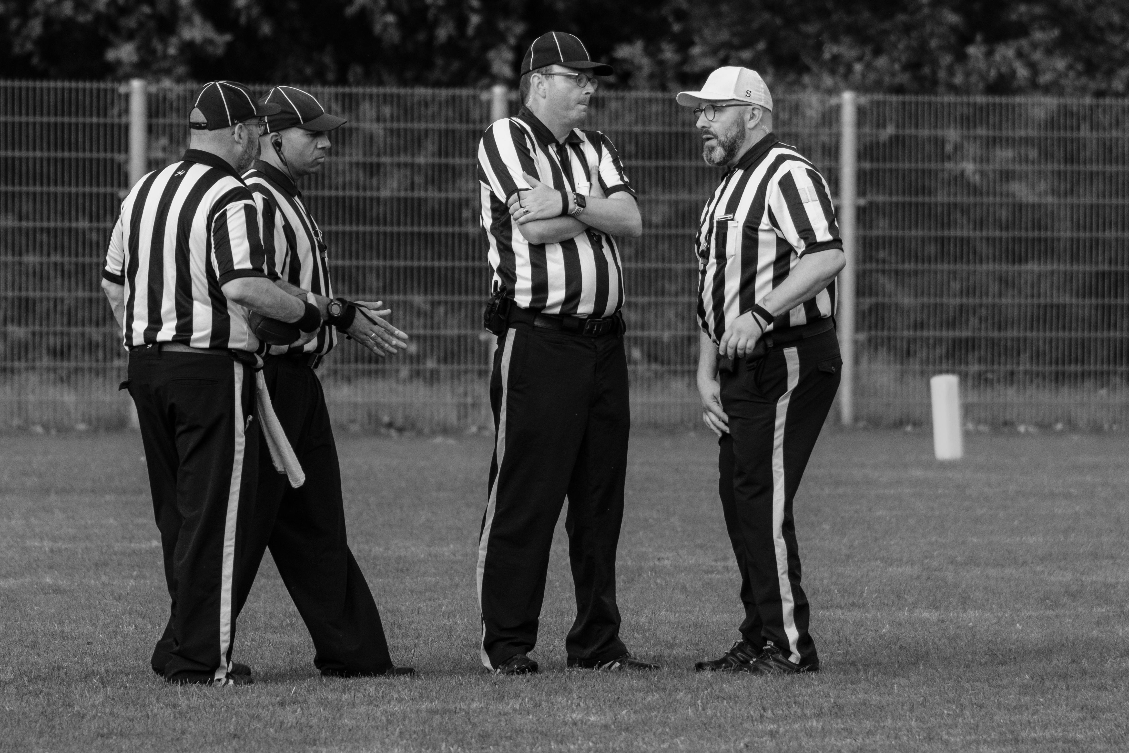 Four referees in striped uniforms discuss on a grassy field.