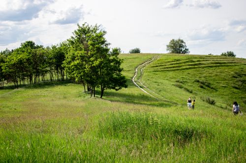 Free Tranquil scene of people walking on lush green hills under a cloudy sky, ideal for nature and outdoor themes. Stock Photo