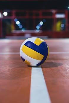 Close-up of a volleyball resting on the line of an indoor court, focus on the ball.
