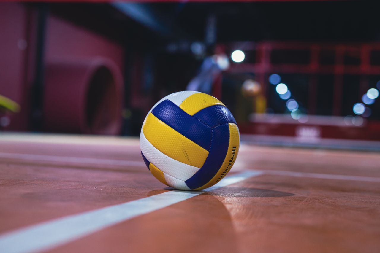 yellow and white volleyball resting on an indoor volleyball court with